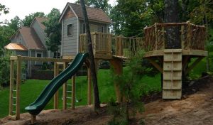 Raised cabin mimics house architecture, with rope bridge to rustic tree deck - Asheville Playgrounds
