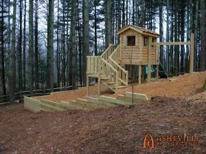 Wooden Playhouse on Hill with Retaining Wall, Slides, Swings, and Stairs - Asheville Playgrounds